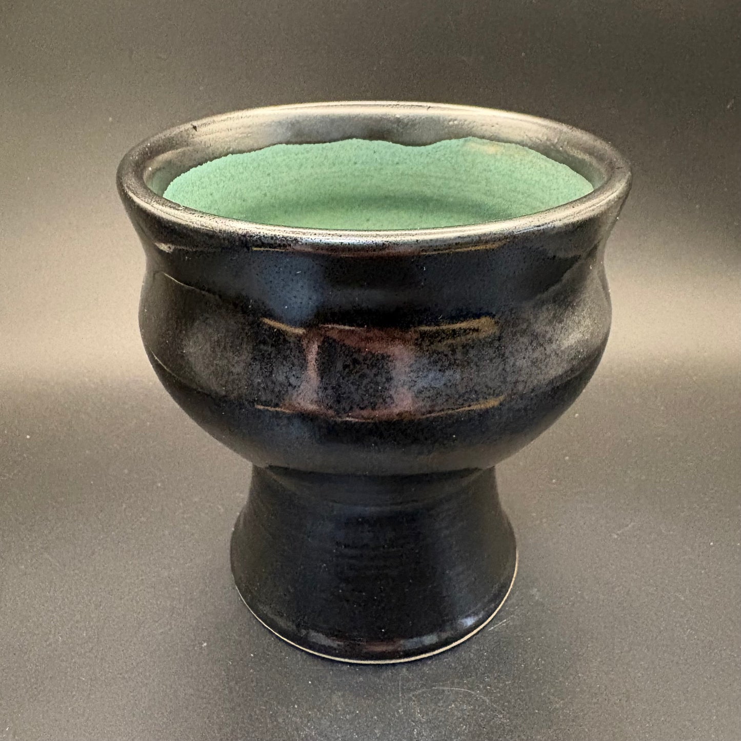 Black ceramic pedestal bowl with green interior on grey background