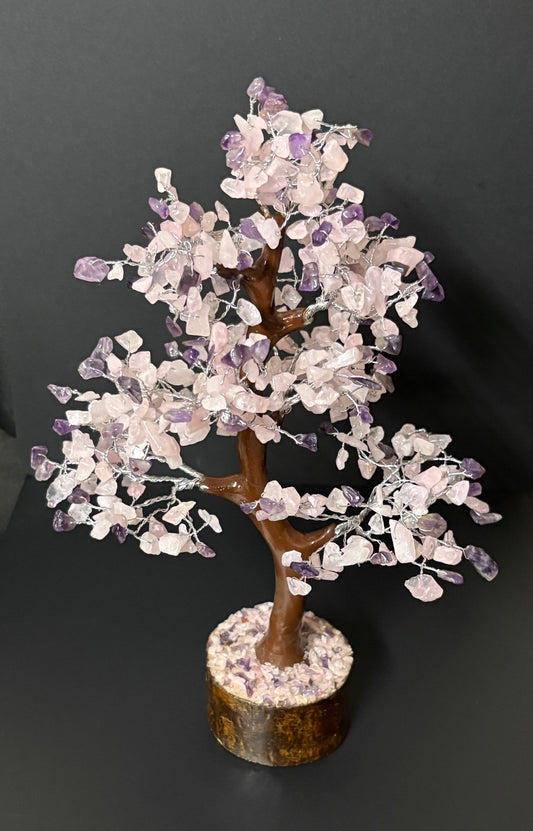 Crystal tree sculpture with rose quartz and purple amethyst leaves on a brown branch structure, set in a circular stone base against a dark gray background.