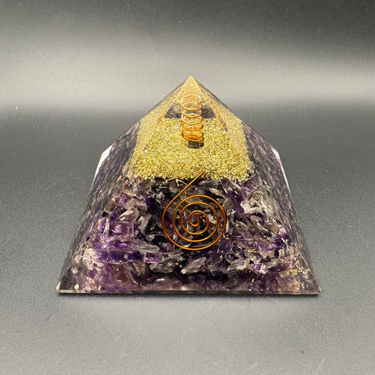 A resin triangular pyramid tower made of layered materials, with a gold glitter top section, Amethyst base, and a copper spiral design on the front, photographed on a dark gray background.