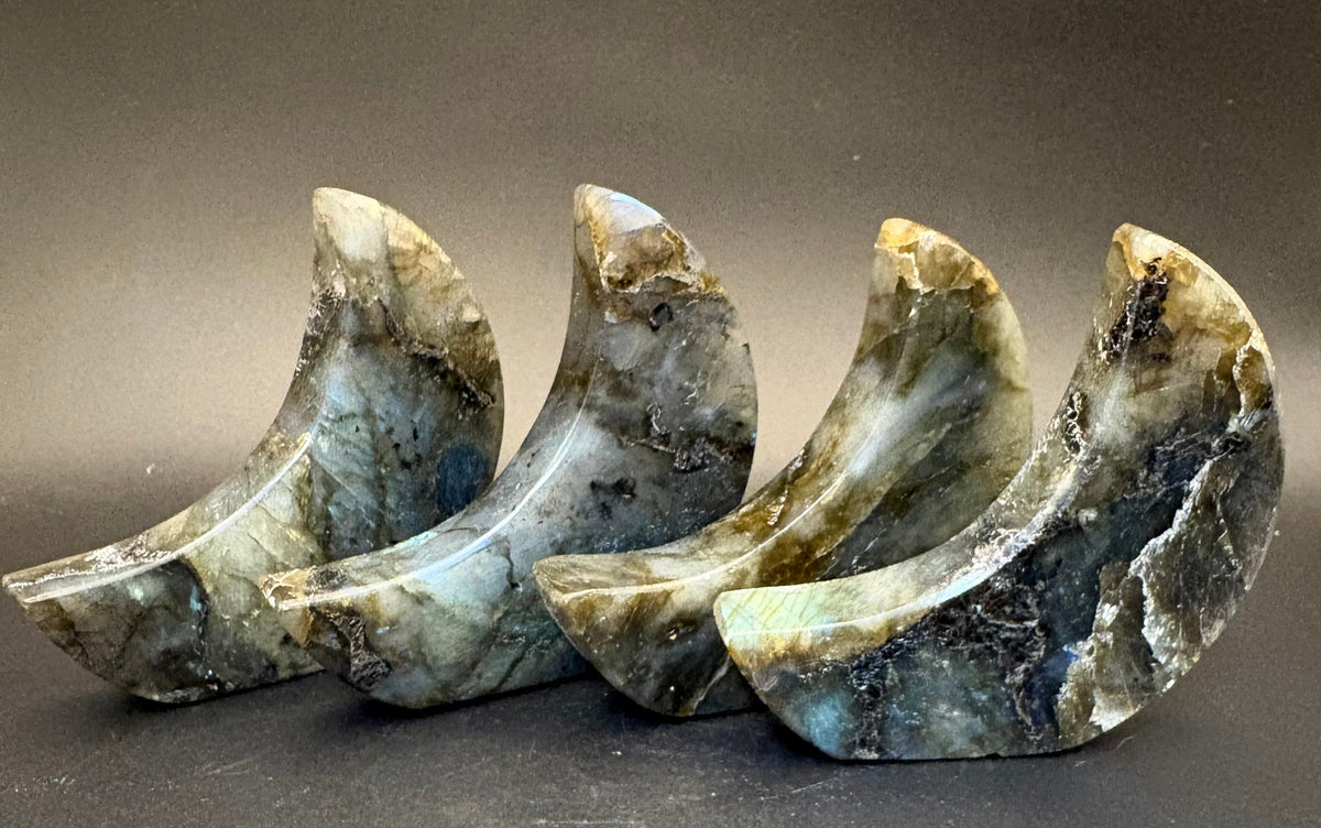 Four polished labradorite crystal moon-shaped holders arranged in a row on a dark gray background.