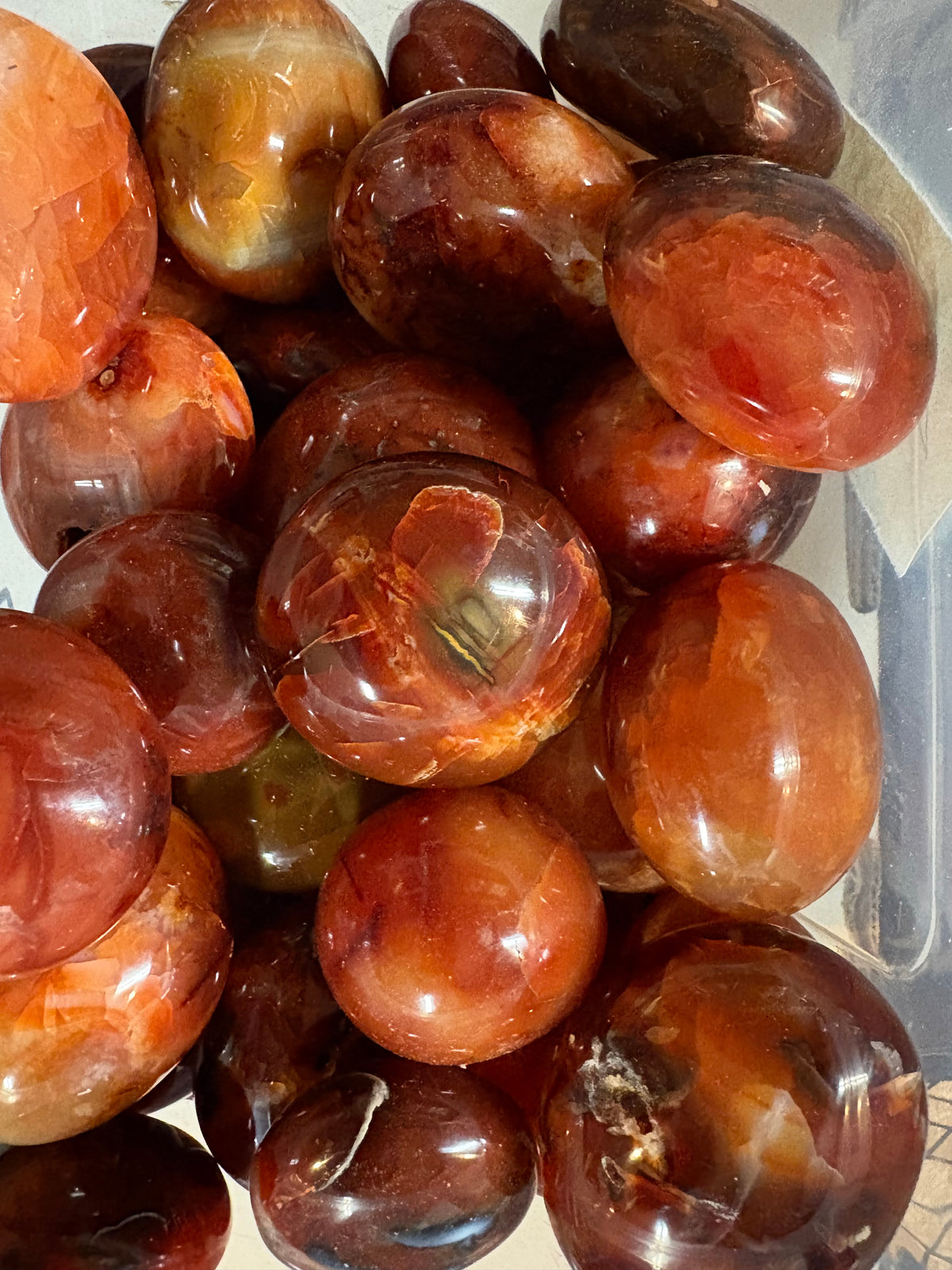 A pile of polished carnelian stones showing natural color variations and some inclusions.