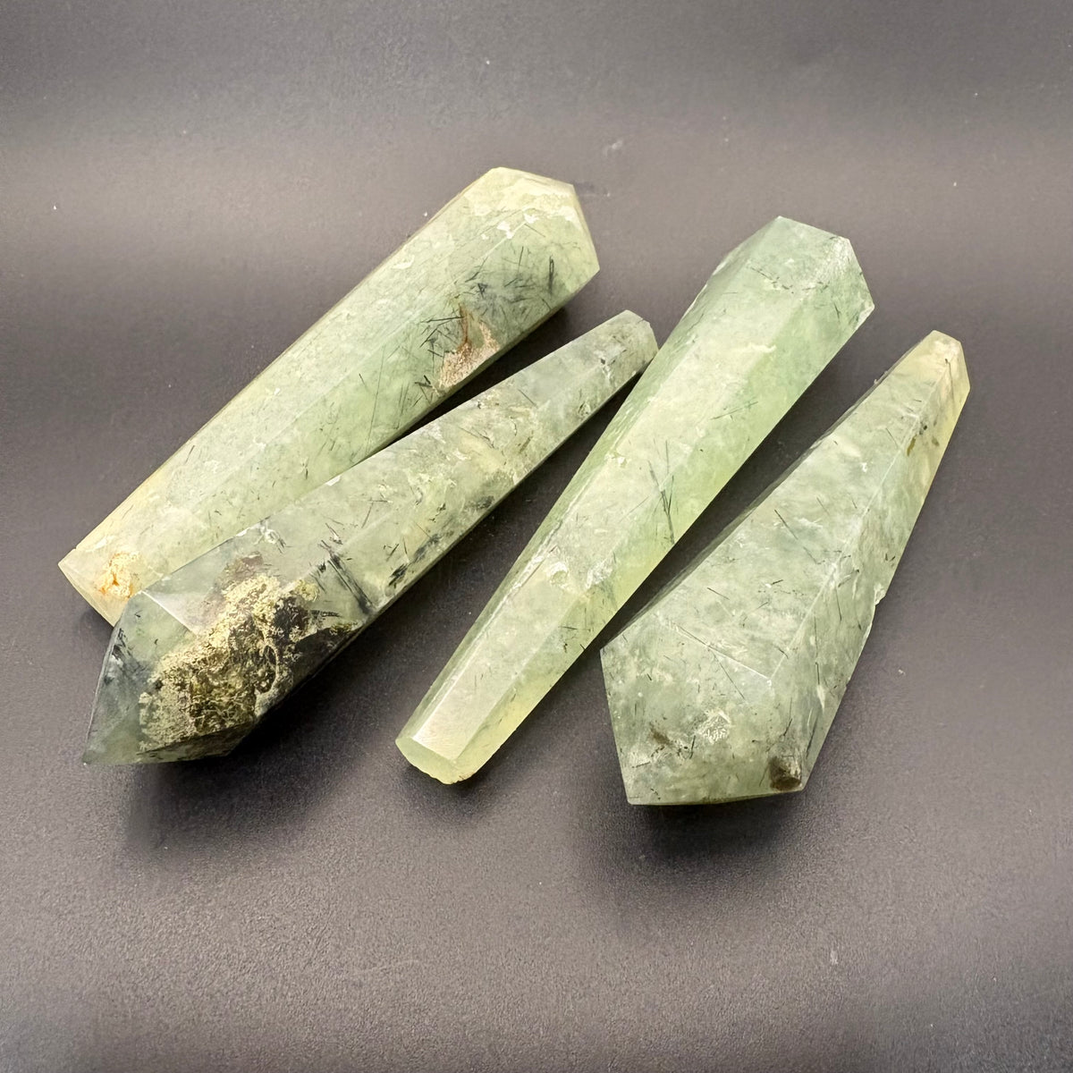 Polished prehnite wands; green with black inclusion on gray background.