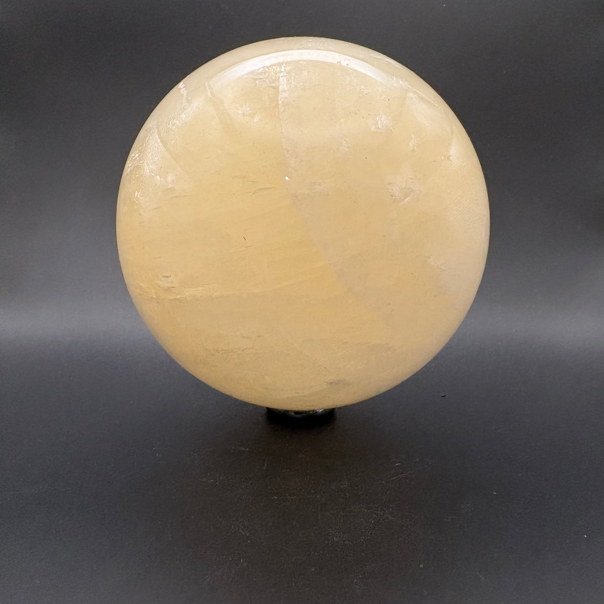 A polished round crystal Citrine sphere  displayed on a small black stand against a dark gray background.