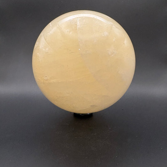 A polished round crystal Citrine sphere  displayed on a small black stand against a dark gray background.