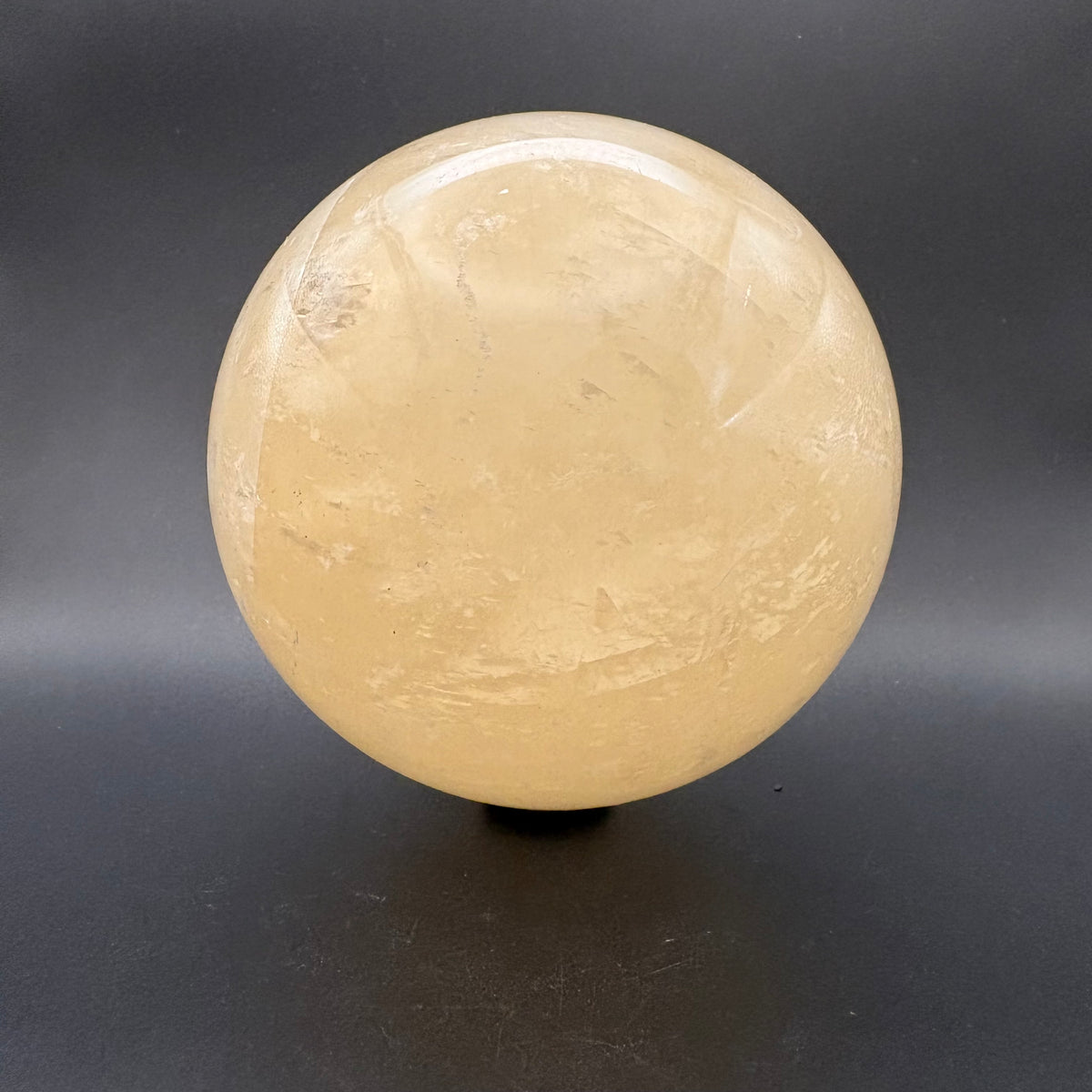 A polished Citrine quartz crystal sphere with natural inclusions, displayed on a small black stand against a dark gray background.