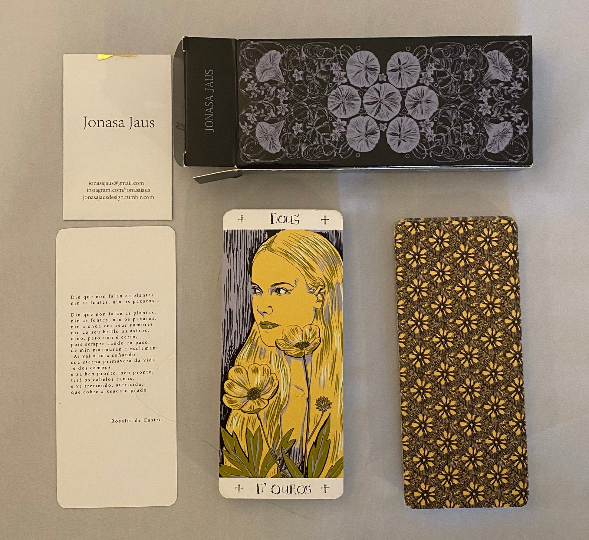 Card with floral design and text, next to a box and another card with a floral pattern on a gray surface.