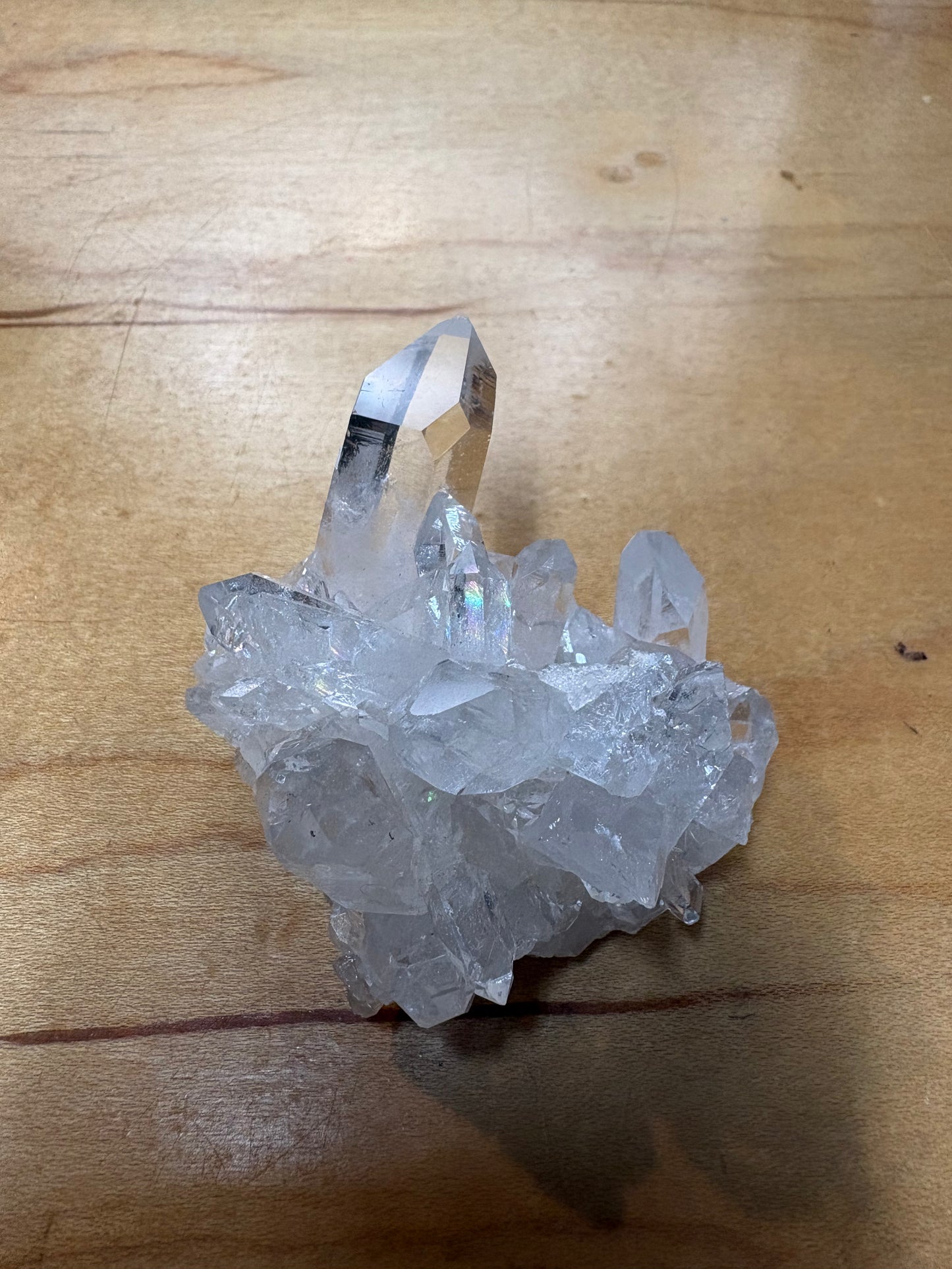 A natural clear quartz crystal cluster with multiple pointed crystal points resting on a light brown wooden surface.