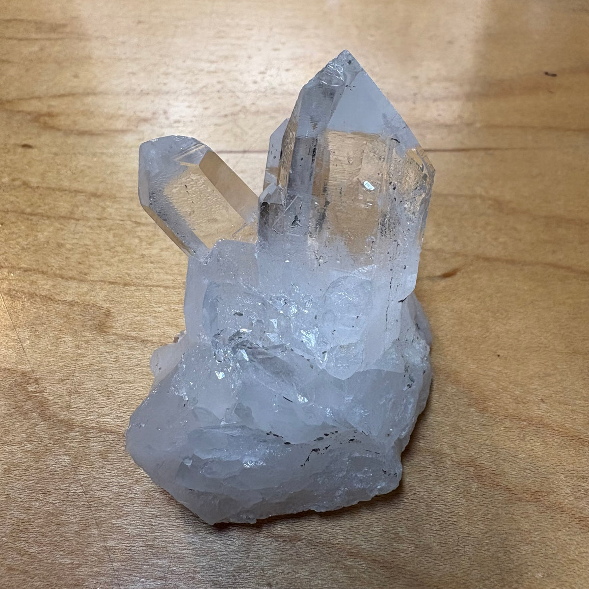 A raw cluster of clear quartz crystals with multiple points, resting on a light brown wooden surface.