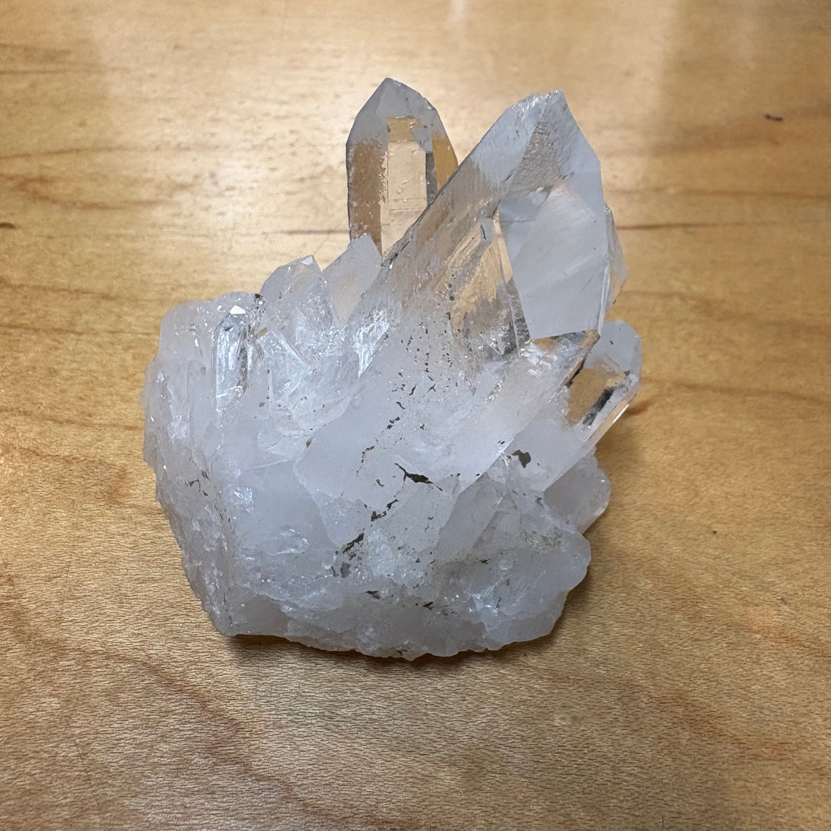 A natural clear quartz crystal cluster with multiple pointed tips, resting on a light brown wooden surface.