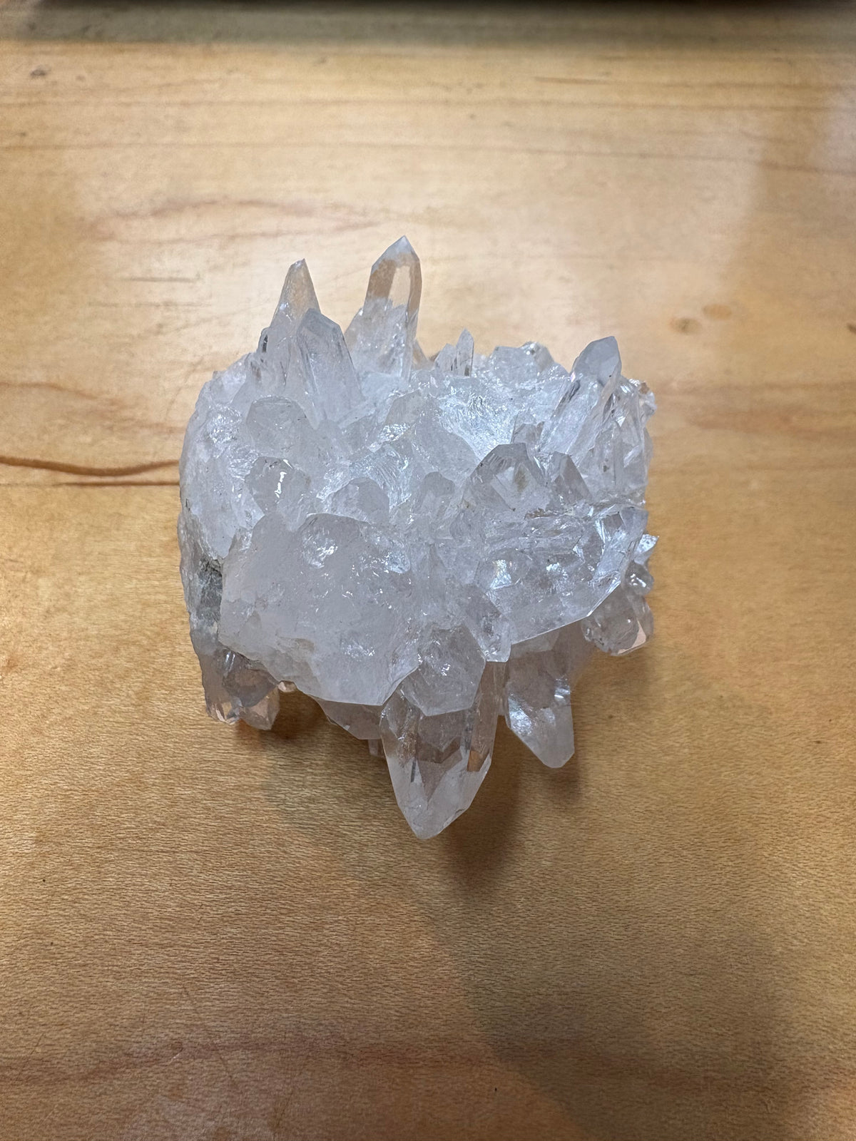 A clear quartz crystal cluster with multiple pointed tips, resting on a light brown wooden surface.