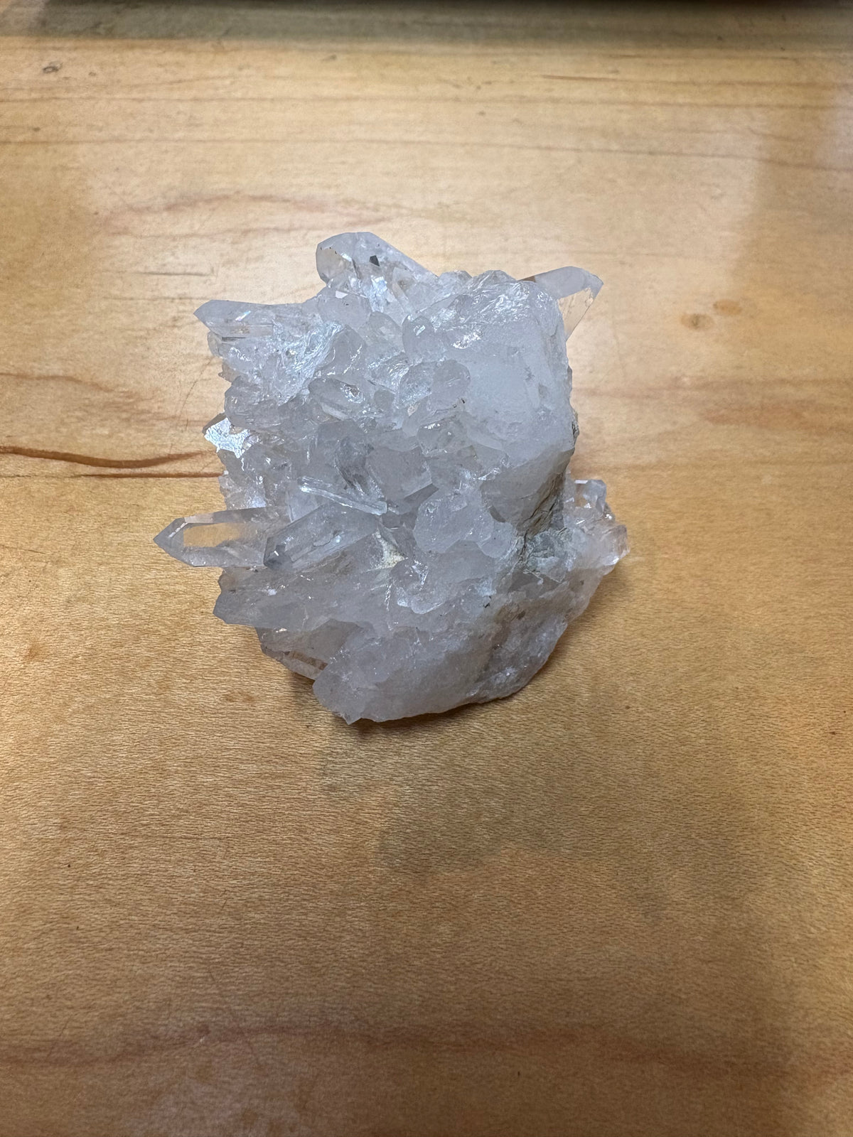 A rough, translucent white crystal cluster resting on a light brown wooden surface.