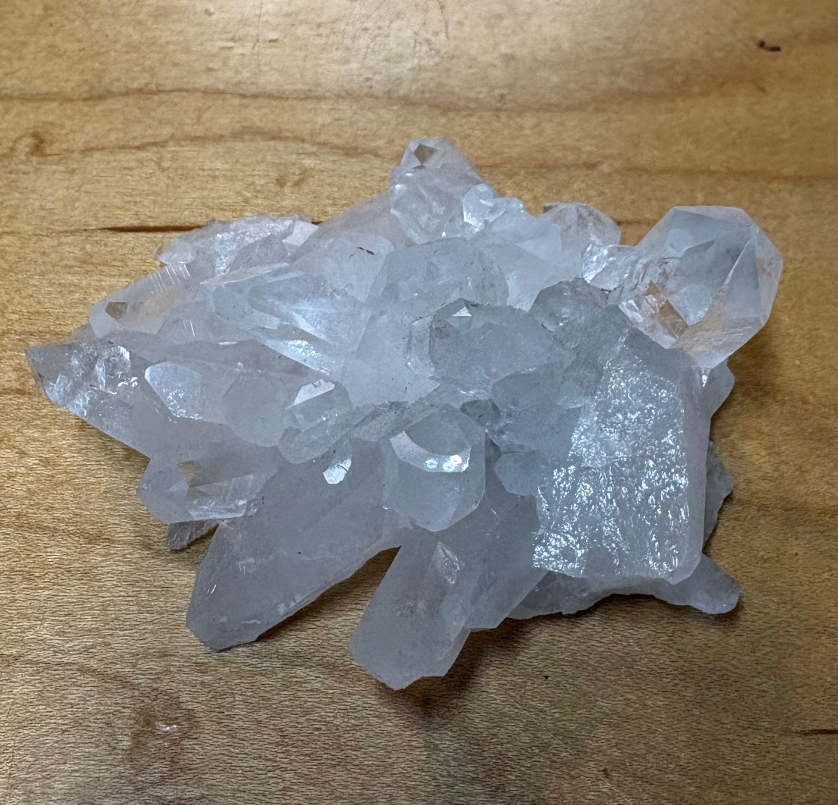 A cluster of translucent white quartz crystal points resting on a light brown wooden surface.