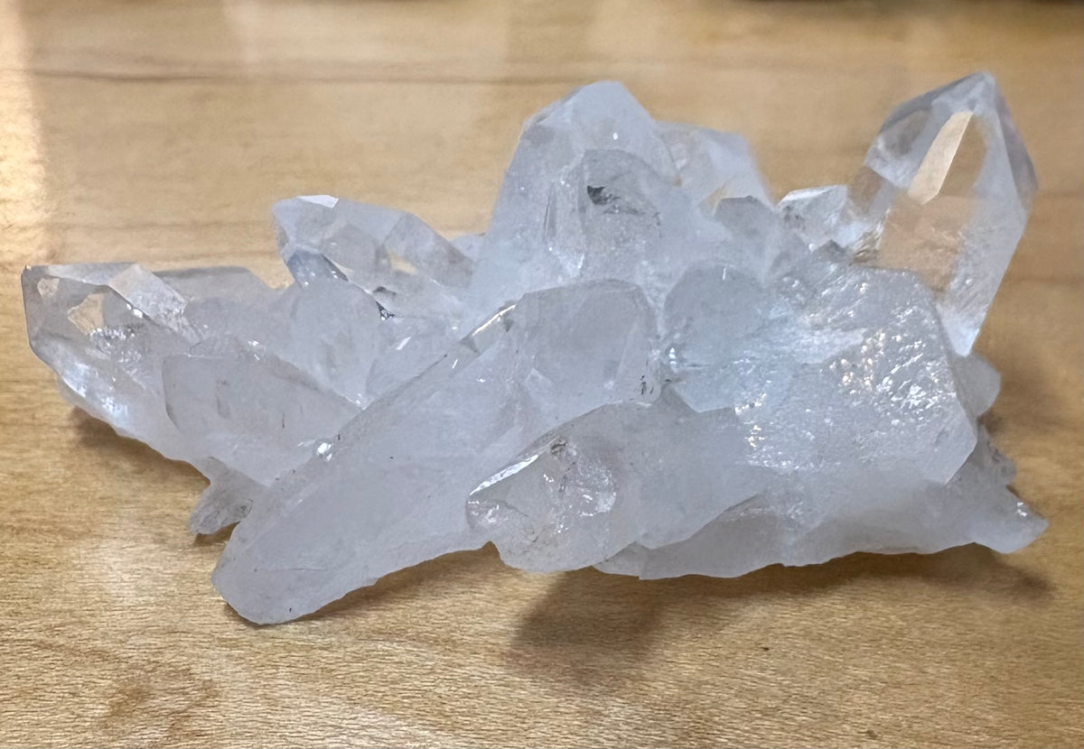A cluster of translucent white quartz crystal points resting on a light brown wooden surface.