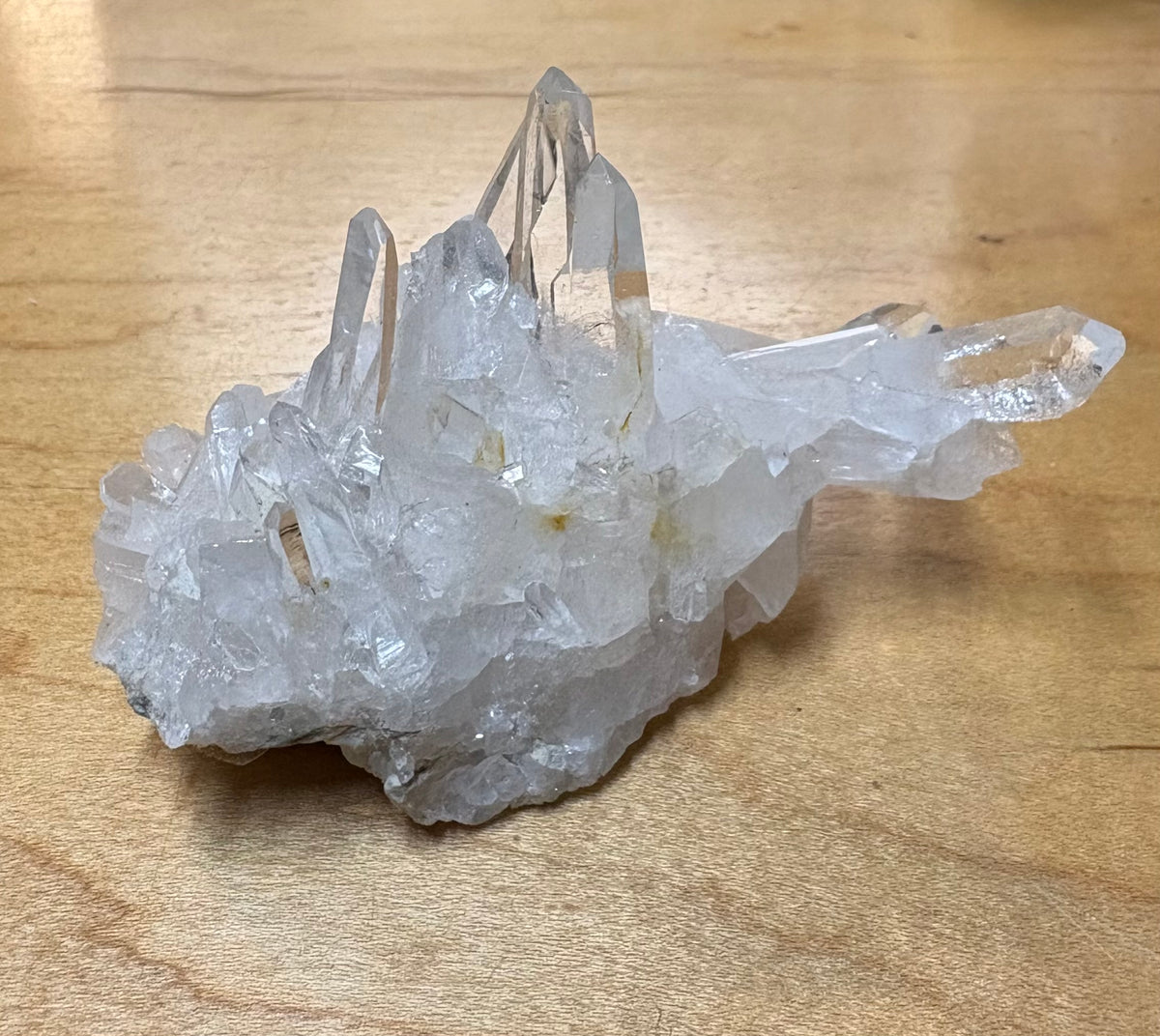 A clear quartz crystal cluster with multiple pointed crystal points on a light brown wooden surface.