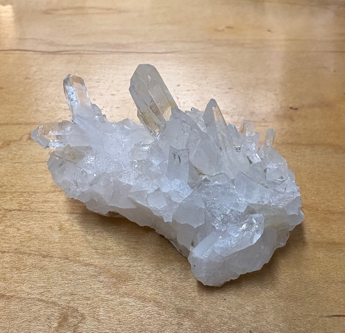 A cluster of clear quartz crystals on a light brown wooden surface.