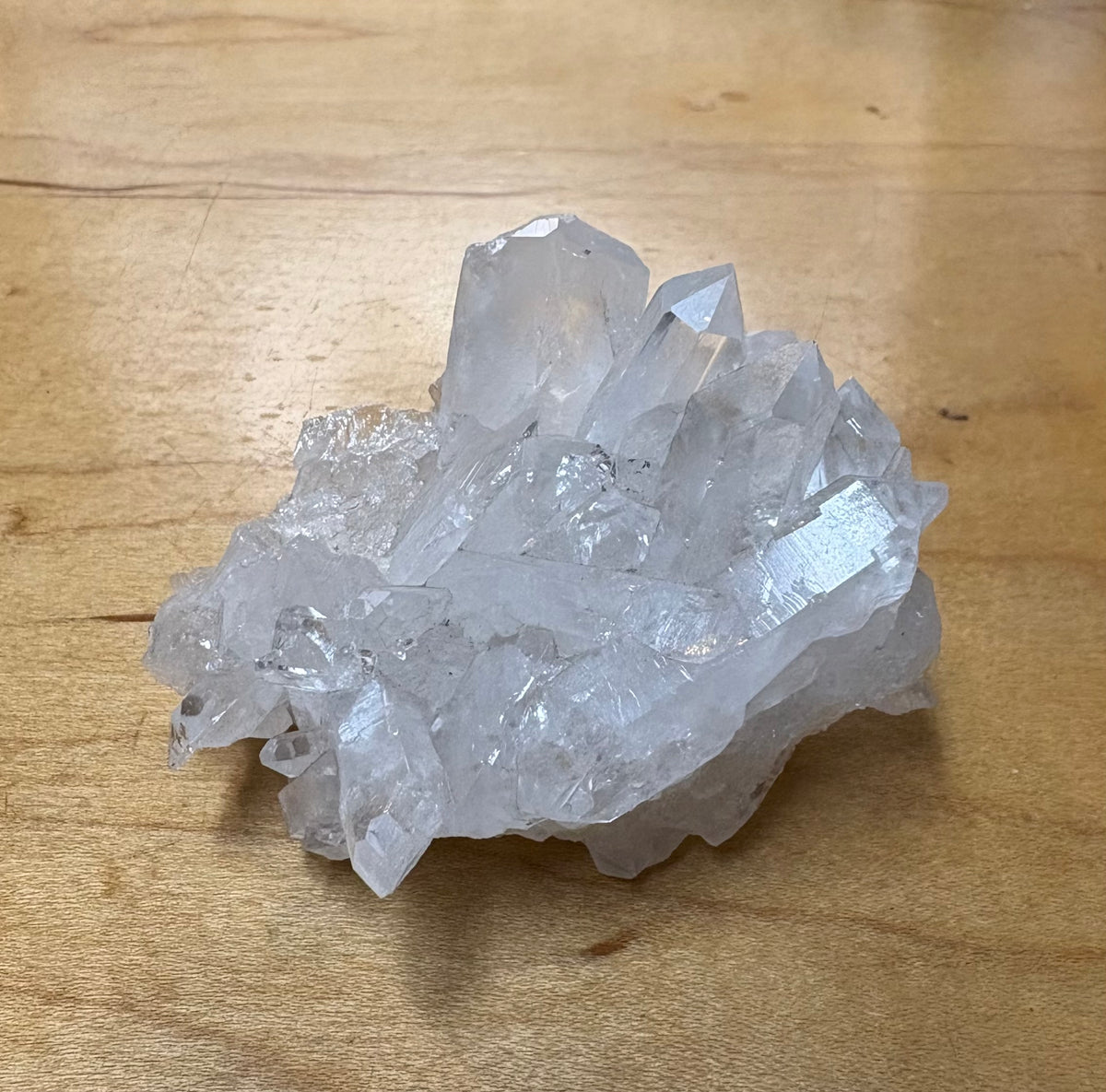 A cluster of clear quartz crystal points resting on a light brown wooden surface.