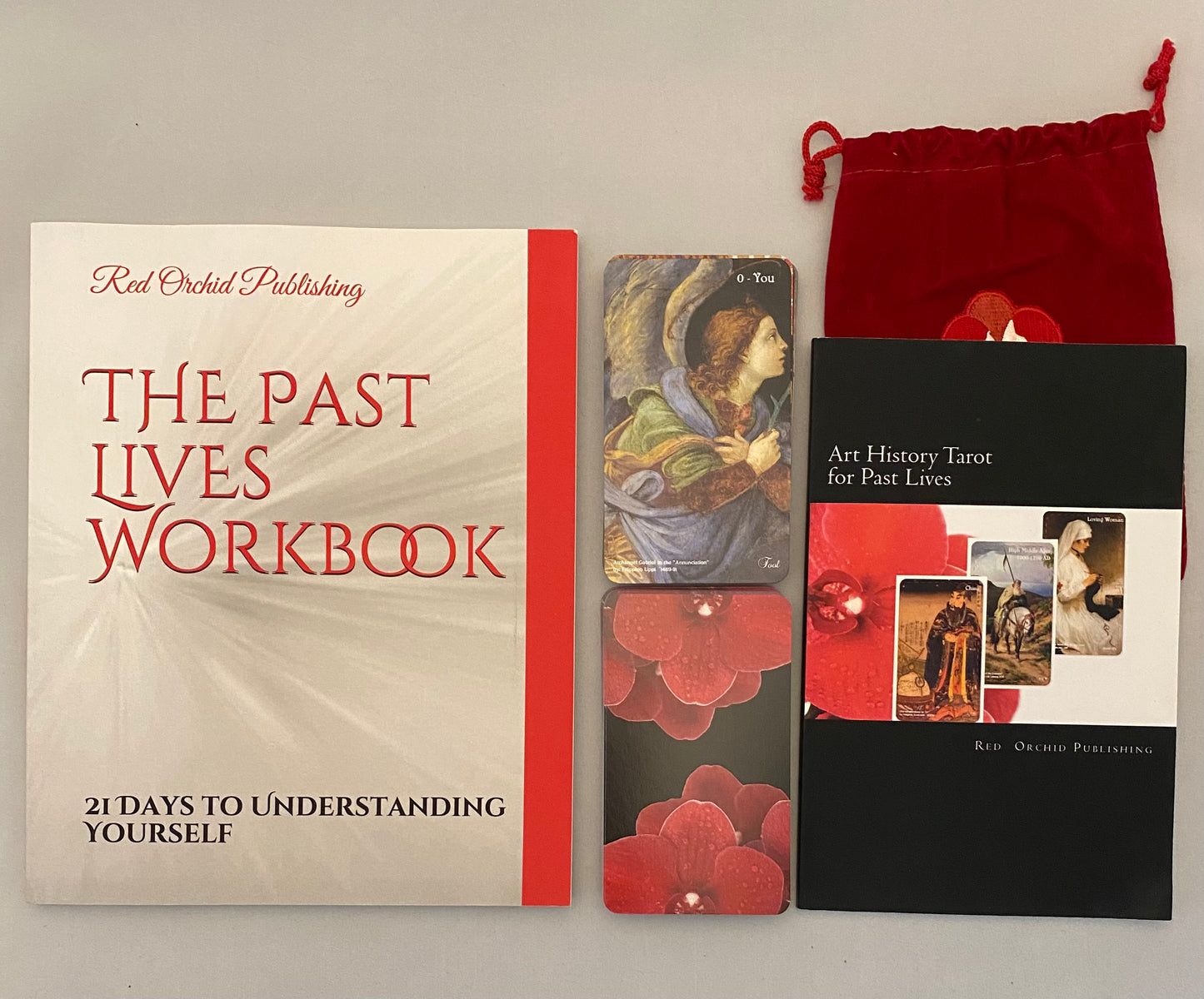 The Past Lives Workbook with tarot cards and a red drawstring bag on a gray background