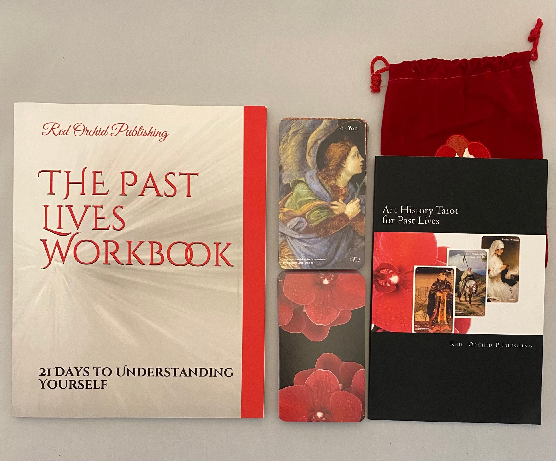The Past Lives Workbook with tarot cards and a red drawstring bag on a gray background