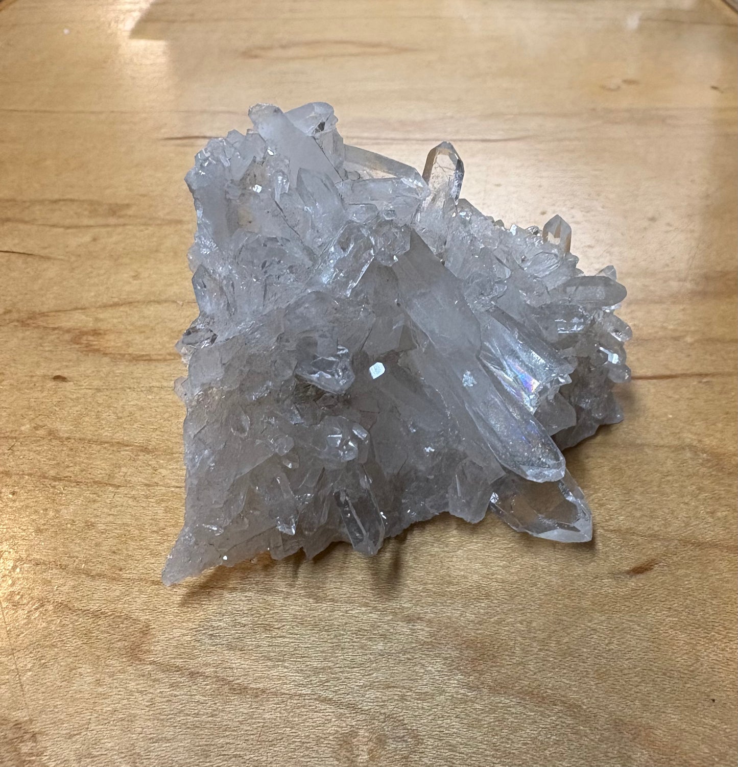 A cluster of clear quartz crystal points resting on a light-colored wooden surface.