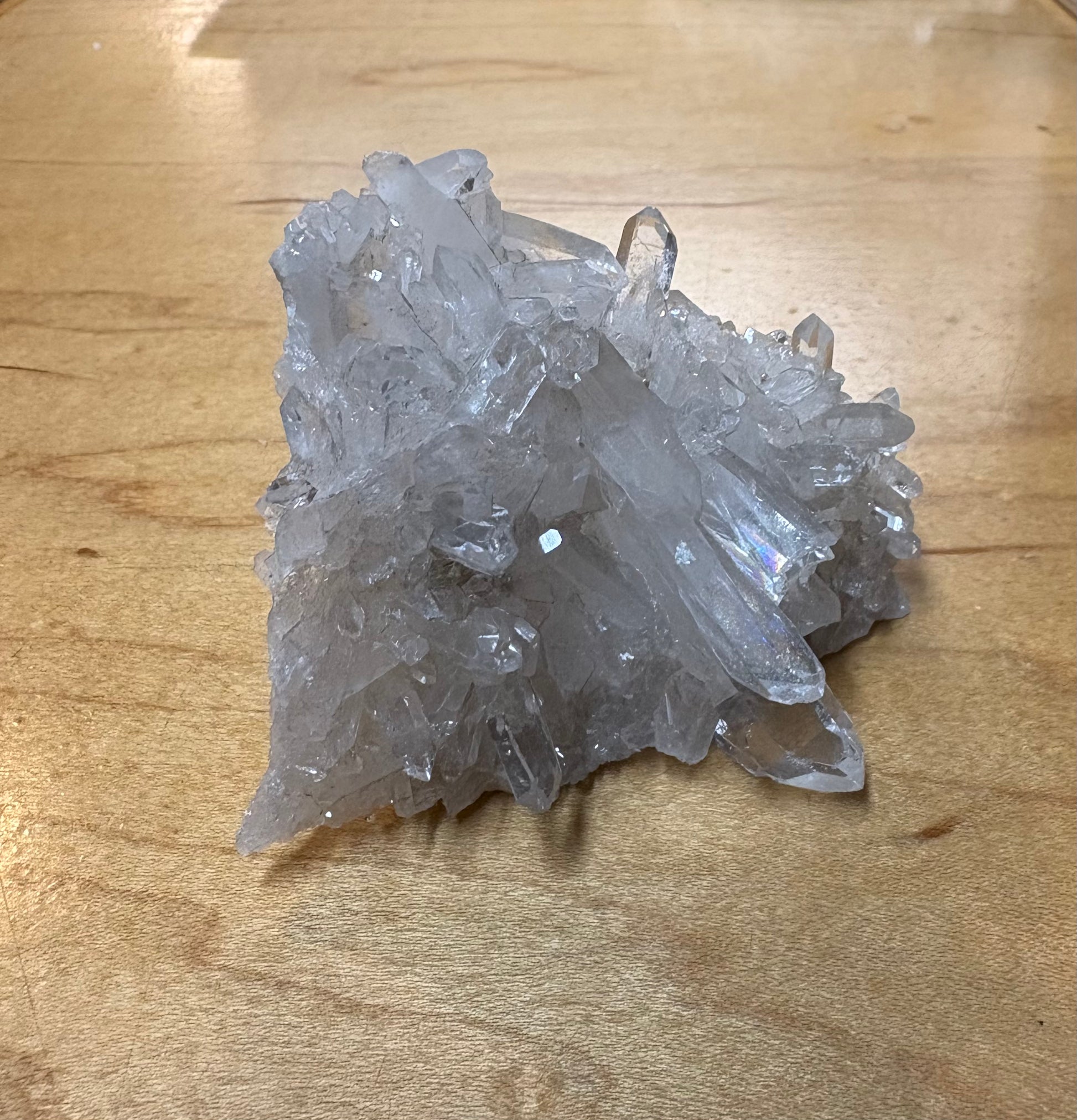 A cluster of clear quartz crystal points resting on a light-colored wooden surface.