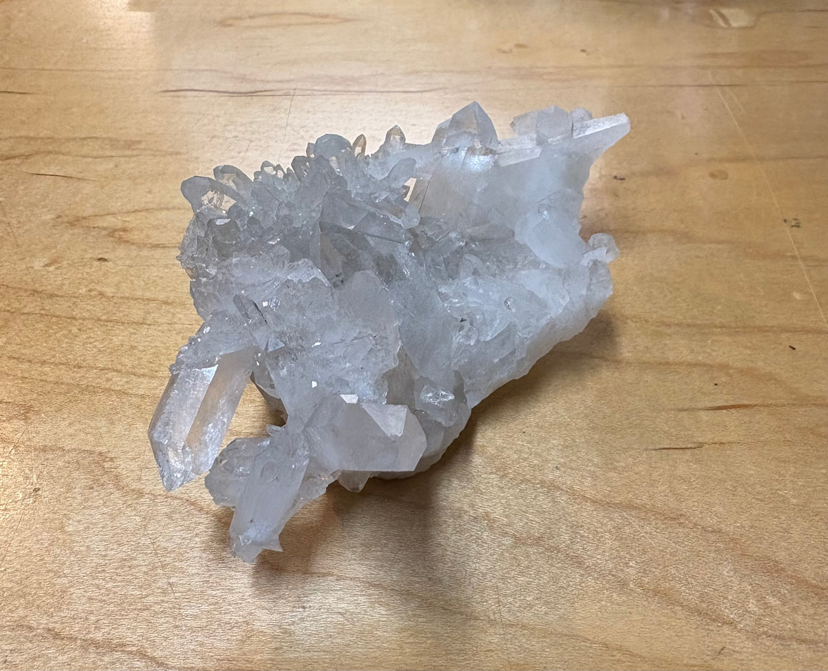 A cluster of translucent white quartz crystals resting on a light brown wooden surface.