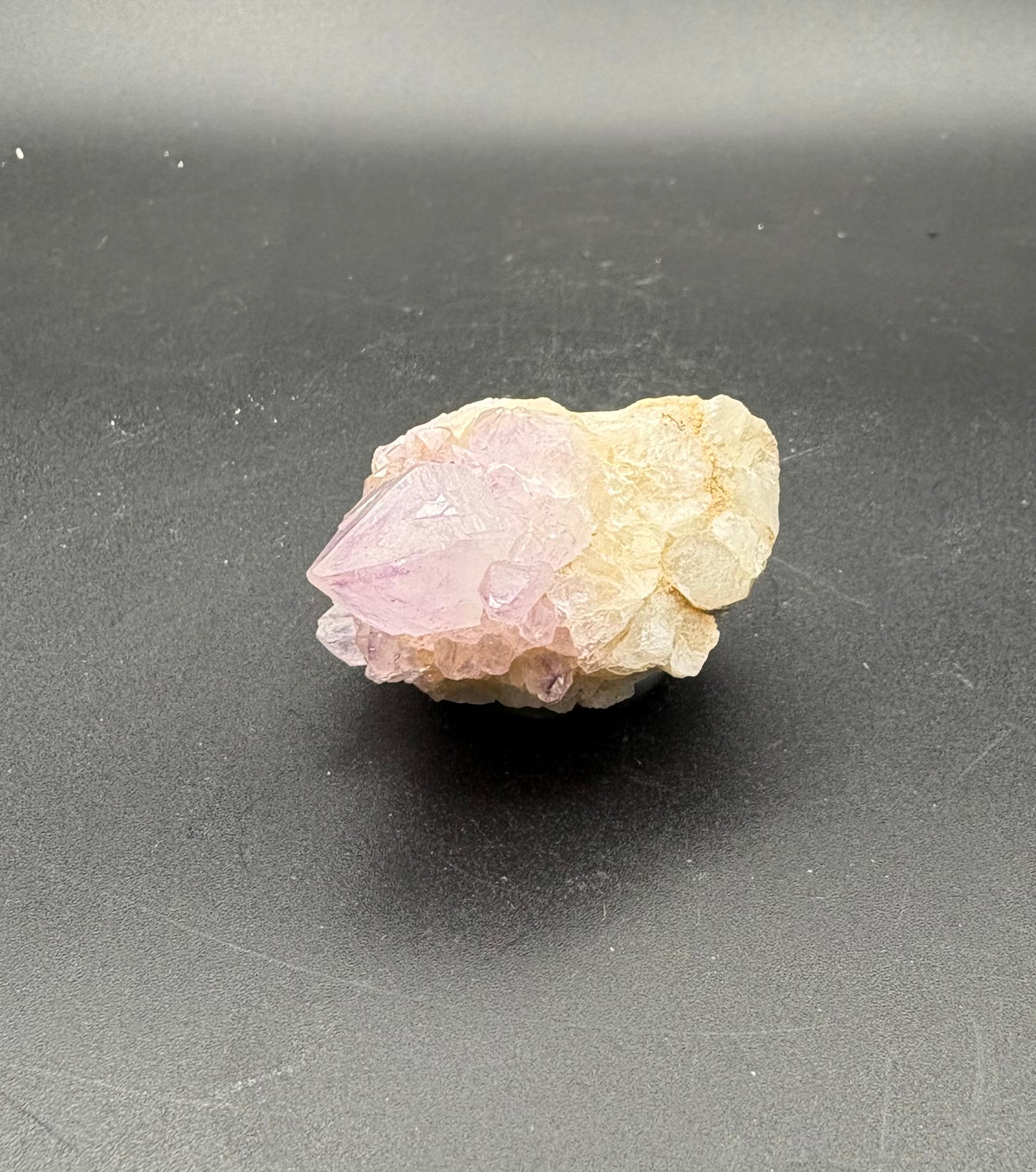 A raw mineral specimen featuring a pink Spirit Crystal point emerging from a pale cream-colored matrix, displayed on a dark gray background.