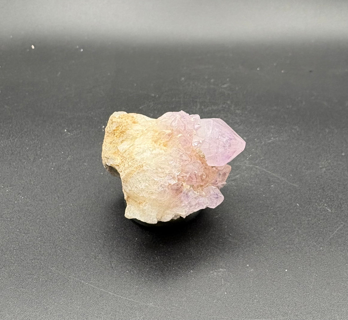 A raw mineral specimen featuring a pink Spirit Crystal point emerging from a pale cream-colored matrix, displayed on a dark gray background.