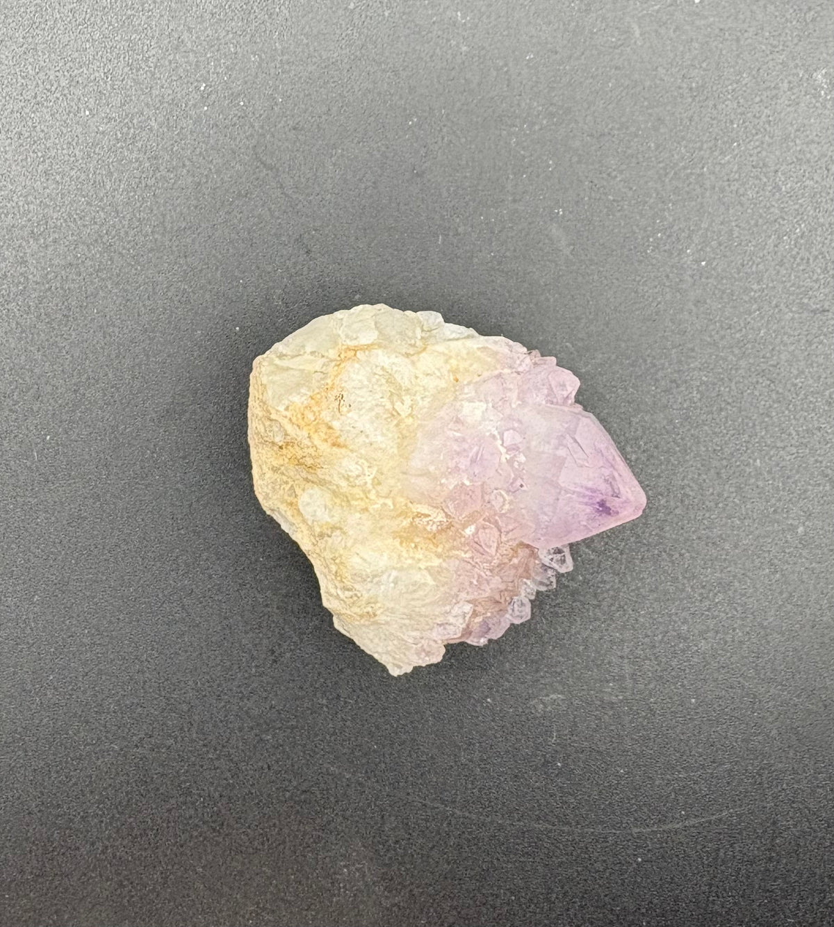 A raw mineral specimen featuring a pink Spirit Crystal point emerging from a pale cream-colored matrix, displayed on a dark gray background.