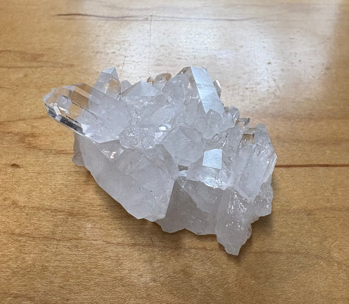 A cluster of clear quartz crystal points resting on a light brown wooden tabletop.
