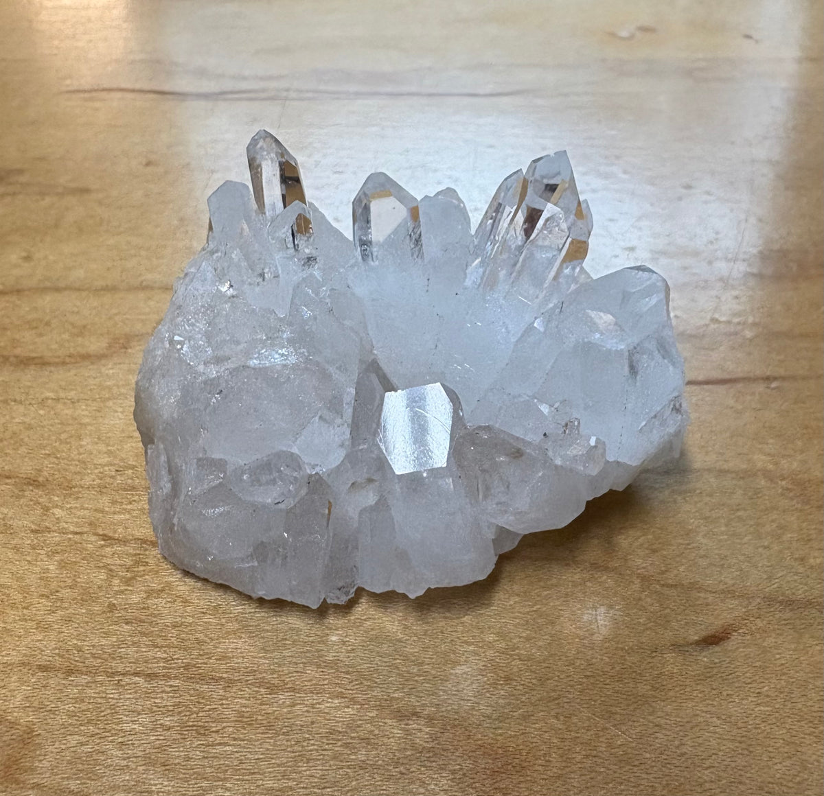 A cluster of clear quartz crystal points resting on a light brown wooden surface.
