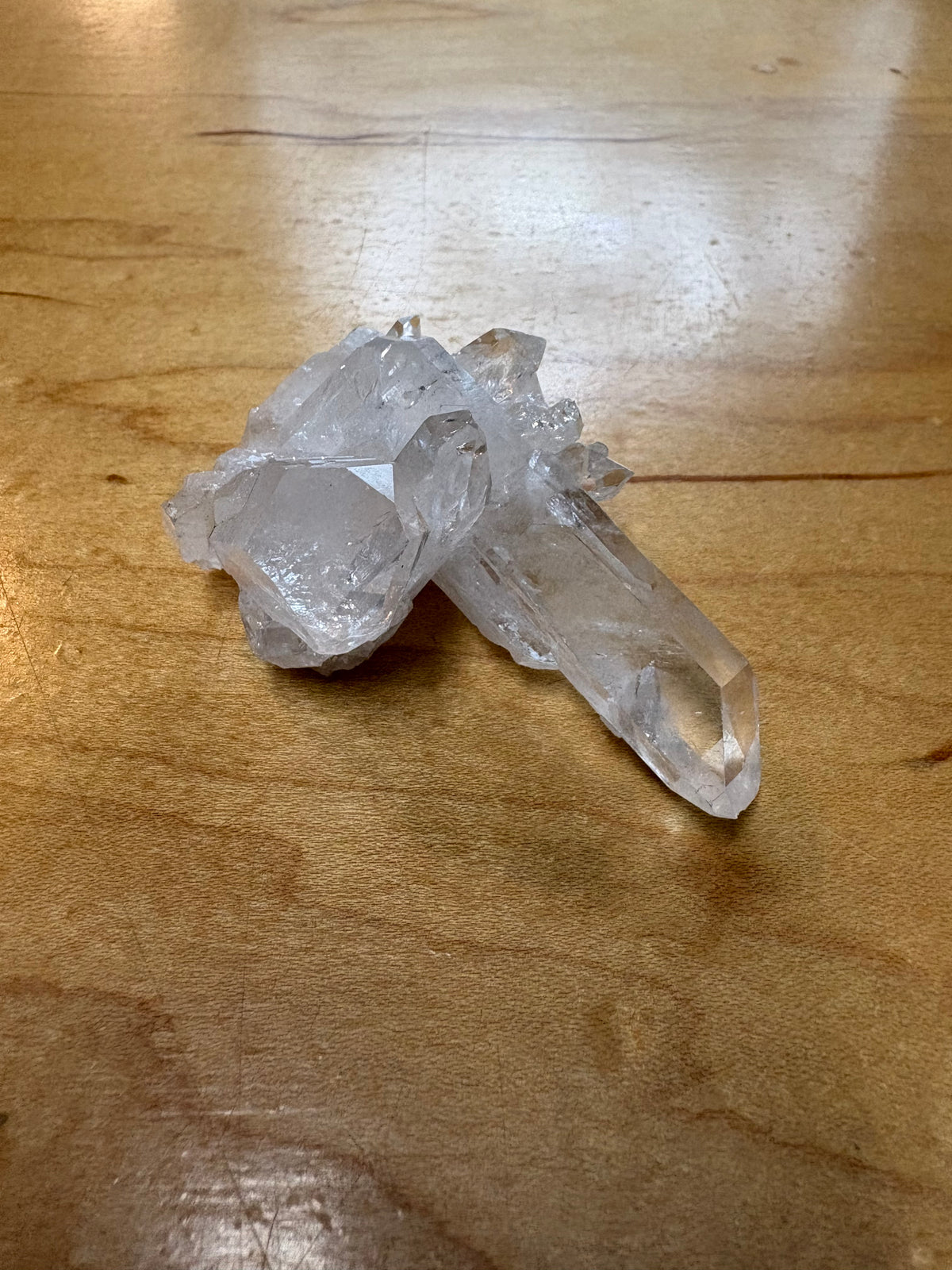 Two clear quartz crystal points resting on a polished wooden tabletop.
