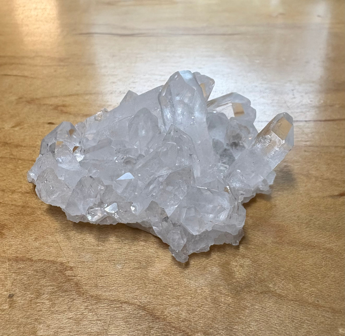 A cluster of clear, translucent quartz crystals resting on a light brown wooden surface.