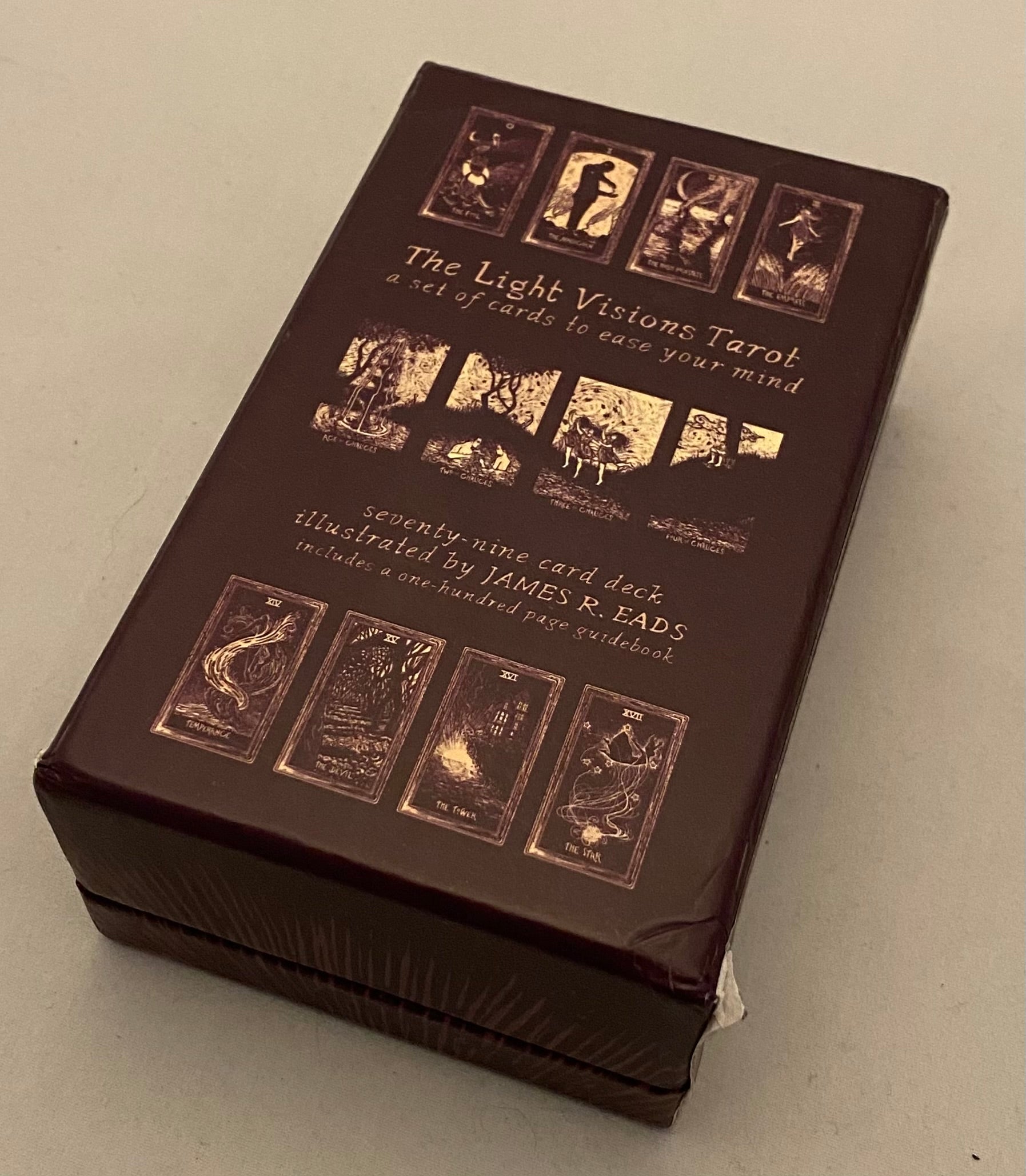 Brown tarot card box with gold illustrations on a light gray background