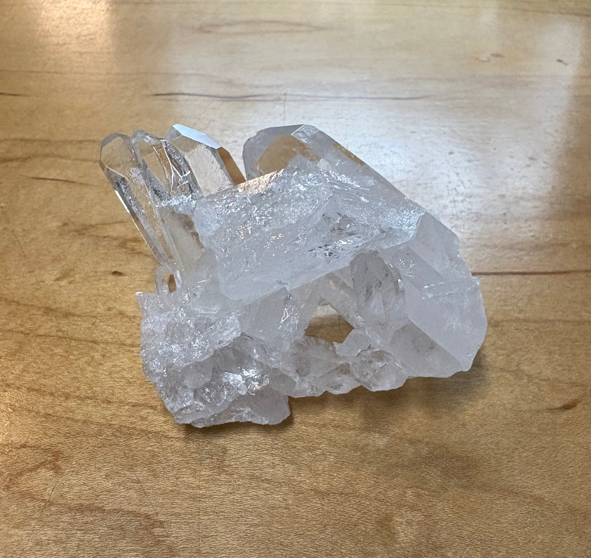 A raw clear quartz crystal cluster with multiple pointed mineral points resting on a light brown wooden tabletop.