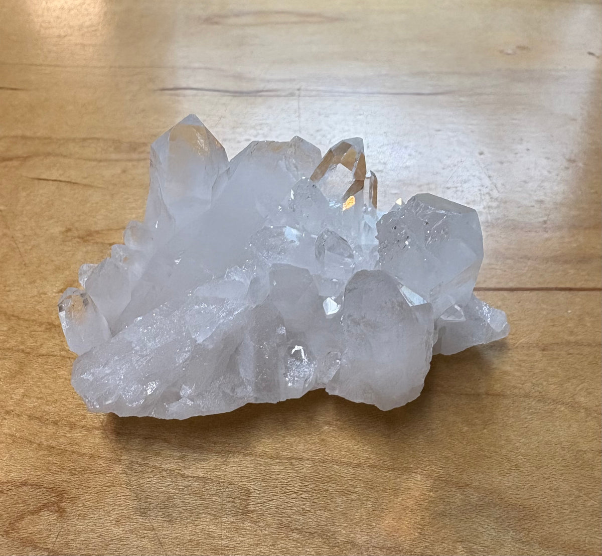 A cluster of natural clear quartz crystals with sharp, faceted points resting on a light brown wooden surface.