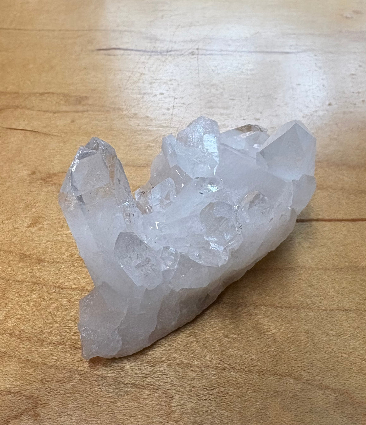 A cluster of natural clear quartz crystals with sharp, faceted points resting on a light brown wooden surface.