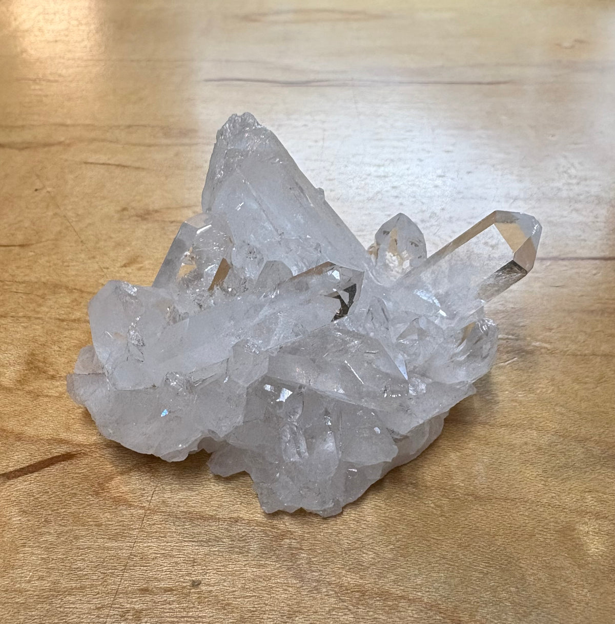 A cluster of natural clear quartz crystal points resting on a light brown wooden surface.