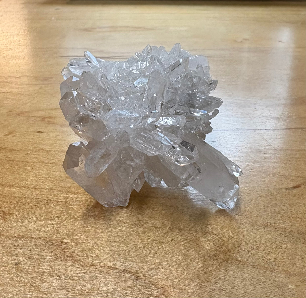 A cluster of clear quartz crystal points resting on a light brown wooden tabletop.