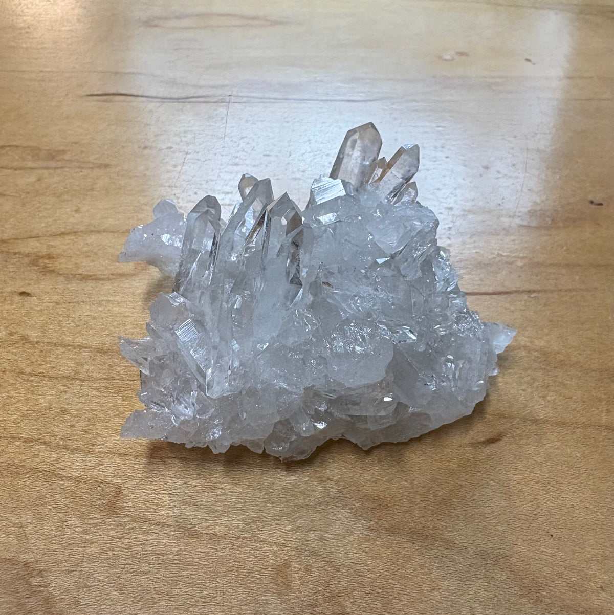 A cluster of clear quartz crystal points resting on a light brown wooden surface.