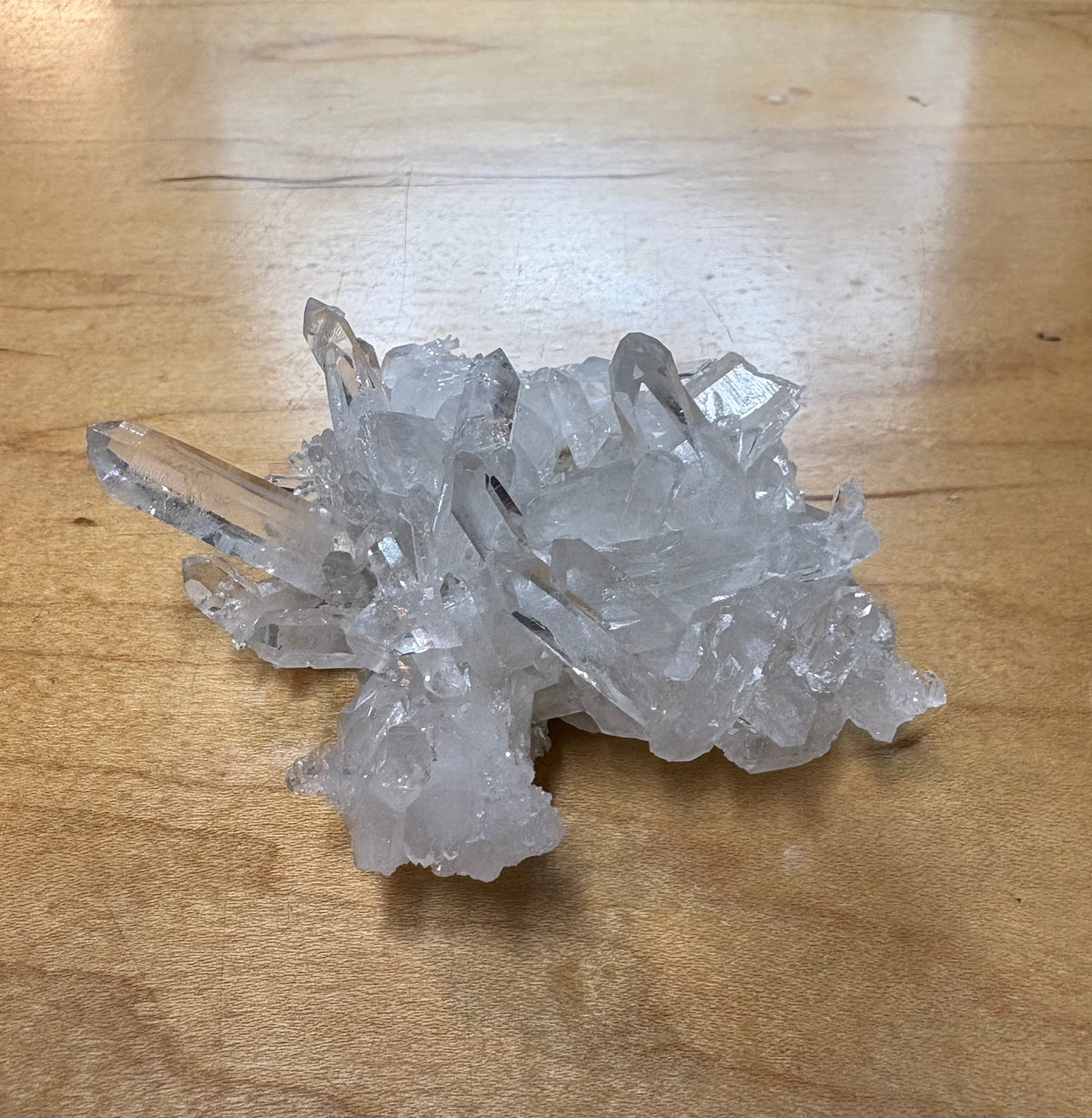 A cluster of clear quartz crystal points resting on a light brown wooden tabletop.