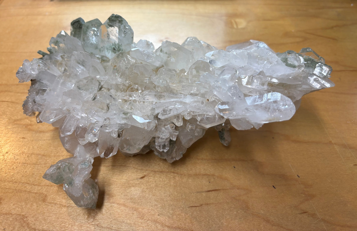 A natural clear quartz crystal cluster with visible internal inclusions, resting on a light brown wooden surface.