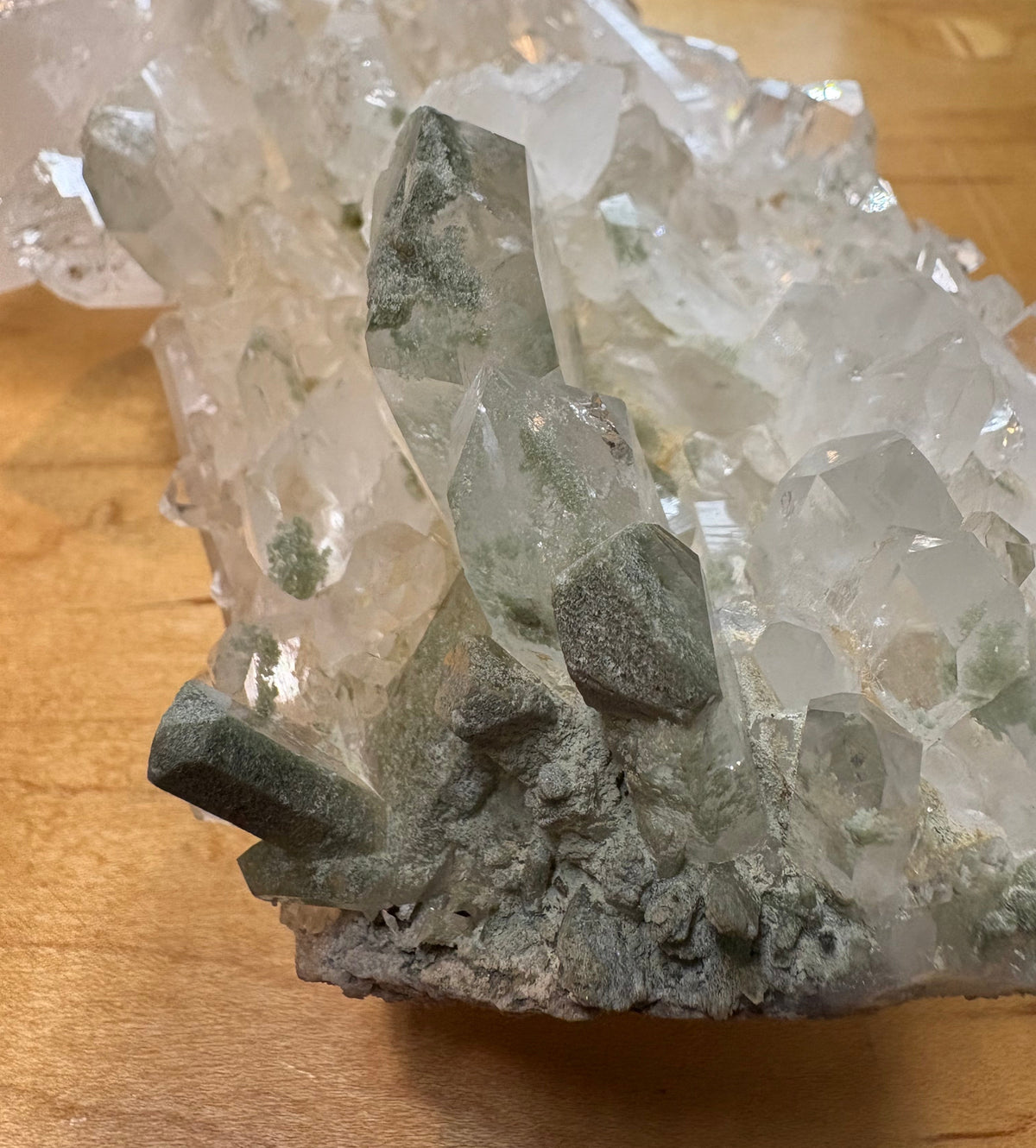 A close-up of a crystal cluster with clear and pale gray translucent points on a rough gray matrix, photographed on a wooden surface.