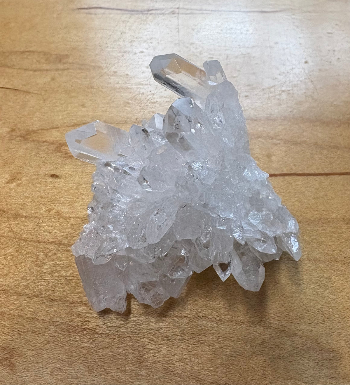 A cluster of clear quartz crystal points resting on a light brown wooden surface.