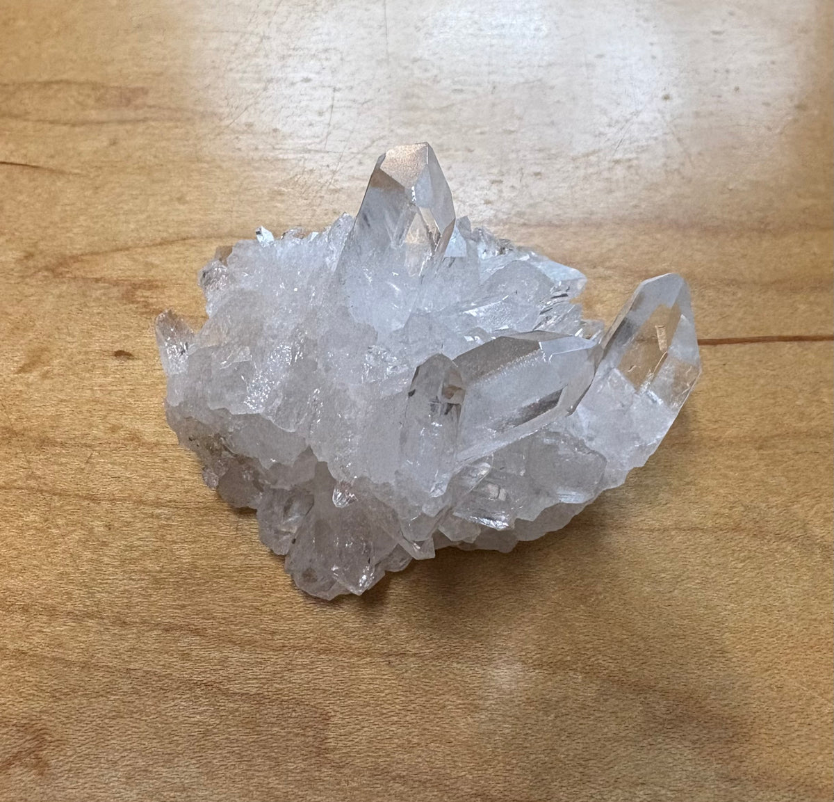 A cluster of clear quartz crystal points resting on a light brown wooden surface.