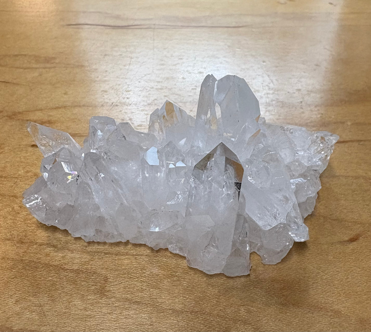 A cluster of clear quartz crystal points resting on a light brown wooden surface.