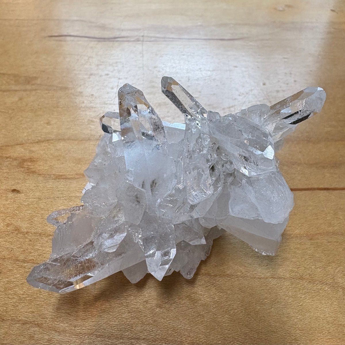 A cluster of clear quartz crystal points resting on a light brown wooden surface.