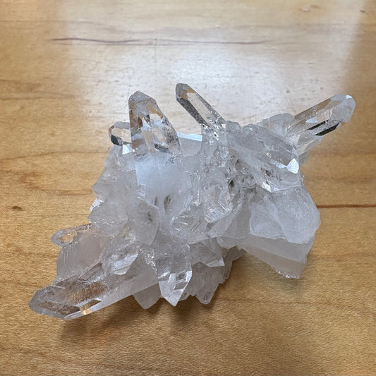 A cluster of clear quartz crystal points resting on a light brown wooden surface.