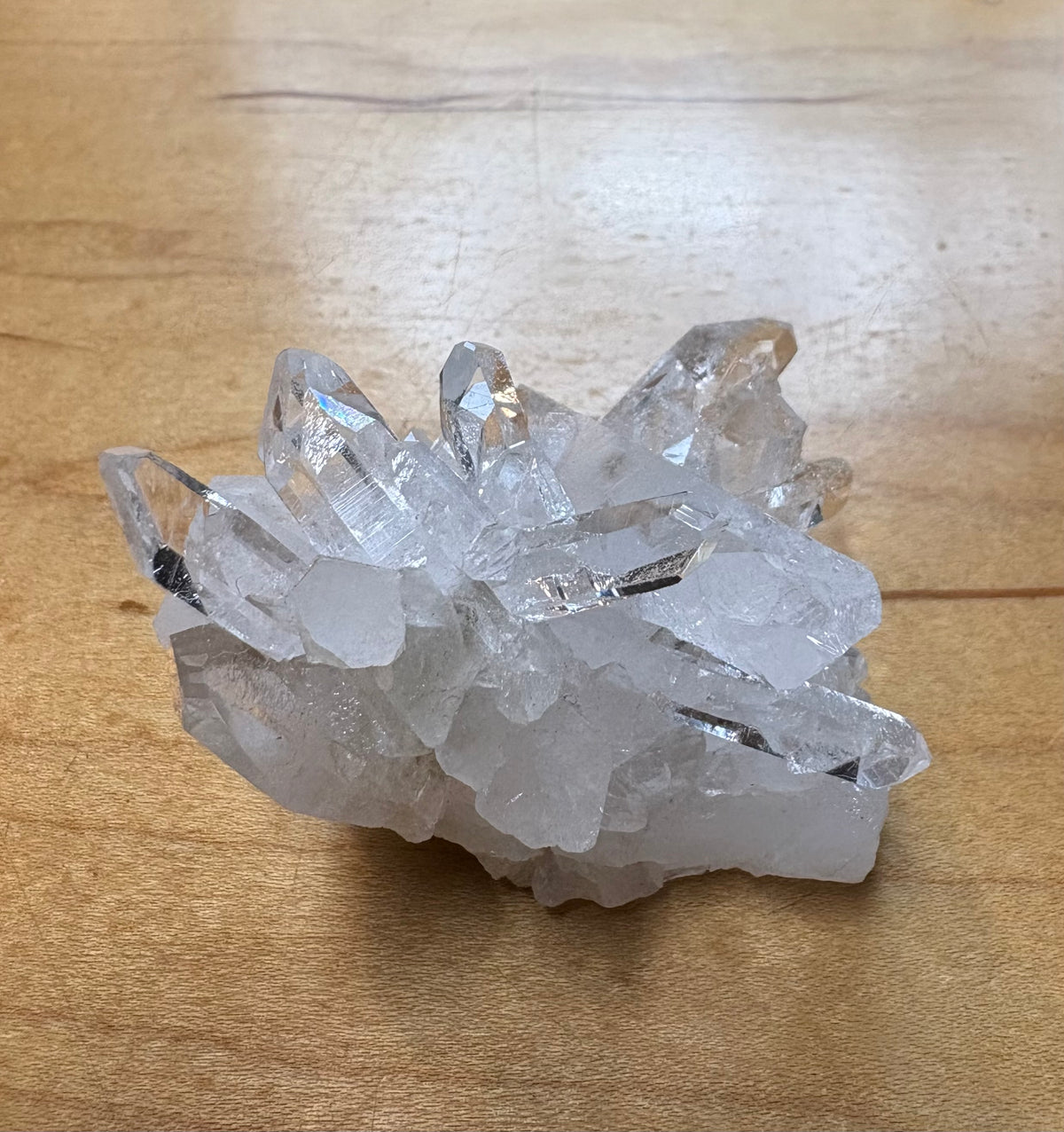 A cluster of clear quartz crystal points resting on a light brown wooden surface.