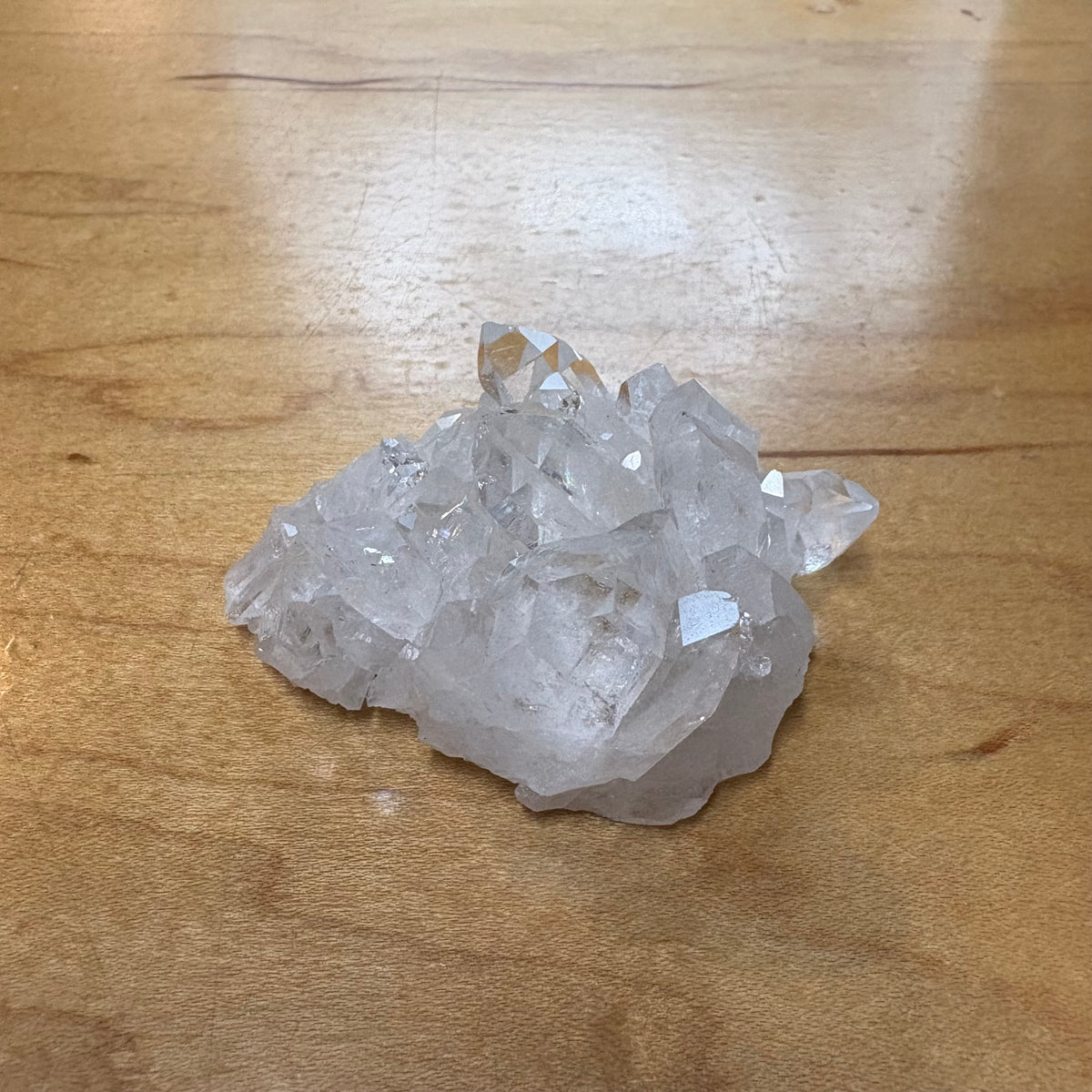 A cluster of clear quartz crystal points resting on a light brown wooden tabletop.