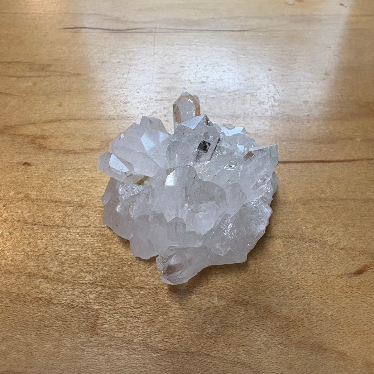 A cluster of natural clear quartz crystals with rough, unpolished points, resting on a light brown wooden surface.